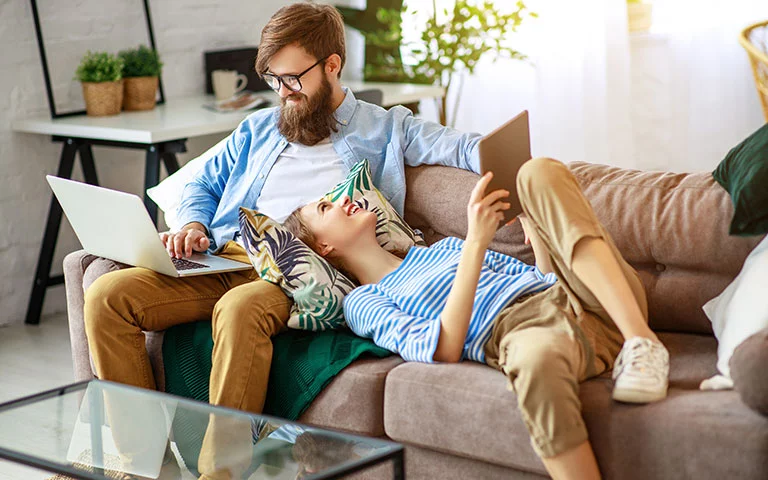 Mann und Frau sitzen mit Laptop und Tablet auf dem Sofa