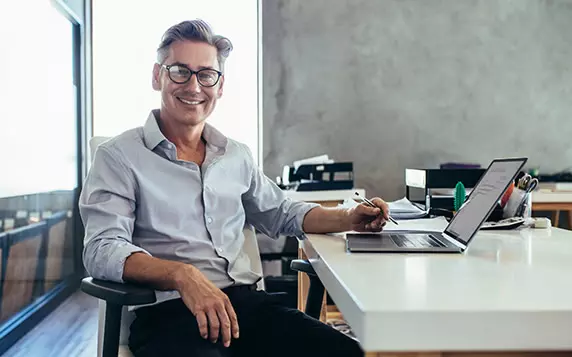 Mann sitzt am Schreibtisch und arbeitet am Laptop