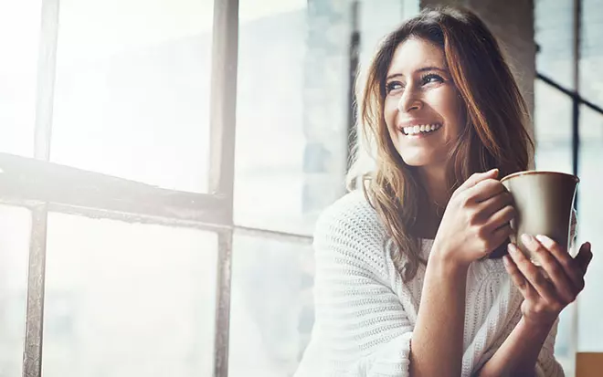 Frau im weißen Pullover hält eine Kaffeetasse