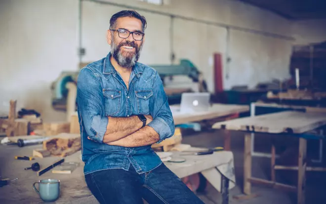 Mann im Jeanshemd lehnt am Tisch in einer Holzwerkstatt
