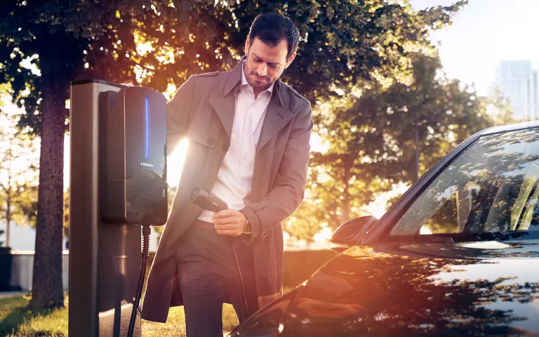 Mann im Trenchcoat lädt ein Elektroauto an einer Wallbox