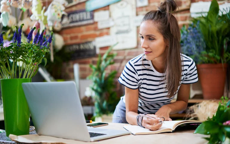 Frau schaut auf einen Laptop, neben dem eine Blumenvase steht