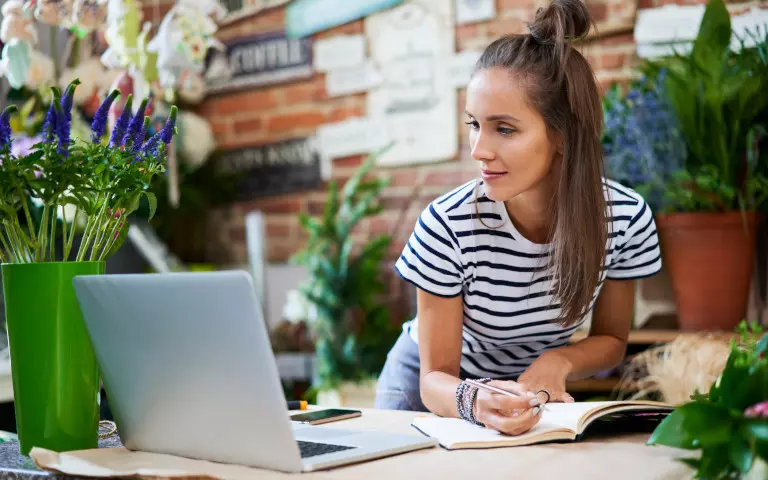 Frau schaut auf einen Laptop, neben dem eine Blumenvase steht