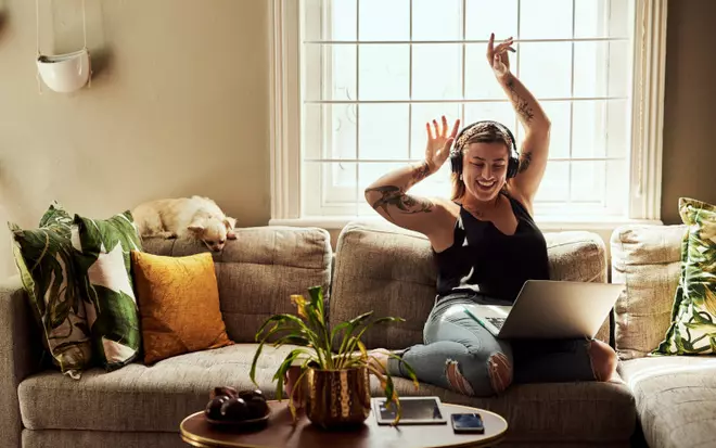 Frau mit Kopfhörer sitzt auf der Couch mit Laptop und Hund