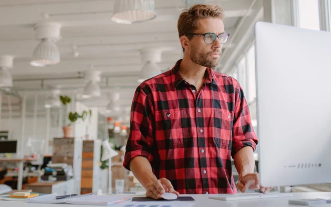 Mann im Karohemd blickt auf einen Monitor