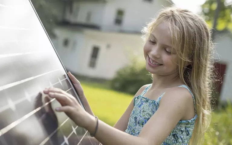 Mädchen im Sommerkleid blickt lächelnd auf ein Solar-Modul