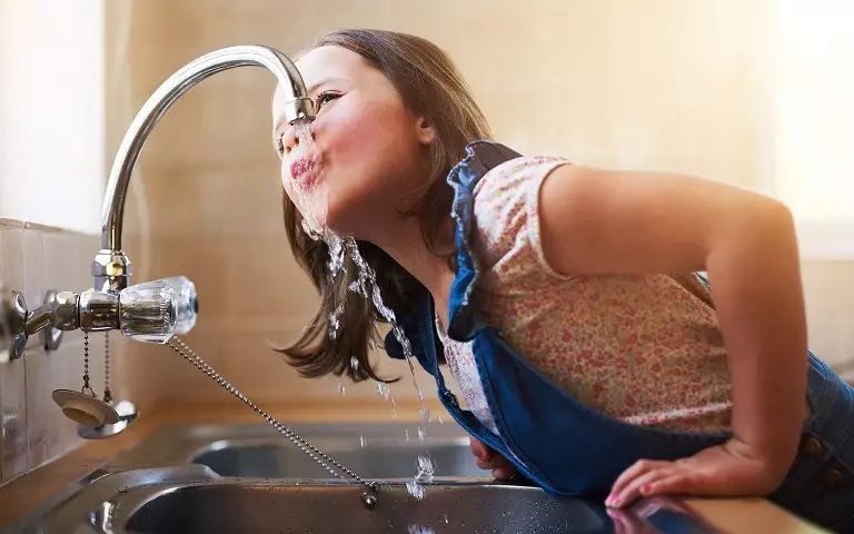 Mädchen trinkt vom Wasserhahn