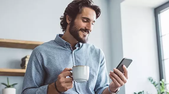 Mann trinkt Kaffee und schaut auf ein Smartphone