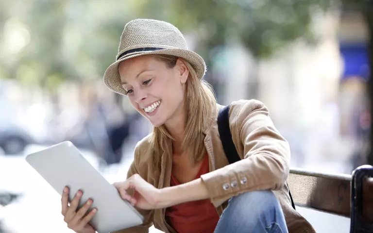 Lächelnde Frau mit Hut schaut auf ein Tablet