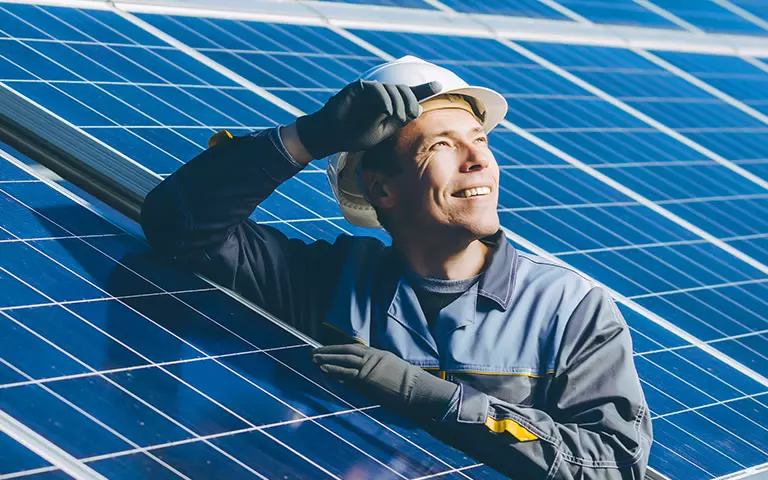 Handwerker steht zwischen Photovoltaik-Anlagen und schaut in die Sonne