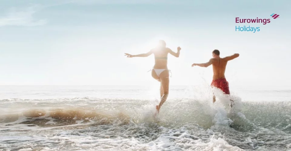 Pärchen läuft in die Meeresbrandung, Eurowings-Logo rechts-oben