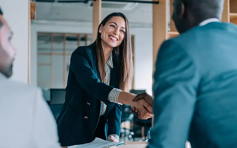 Frau im eleganten Business-Outfit gibt einem Kunden die Hand